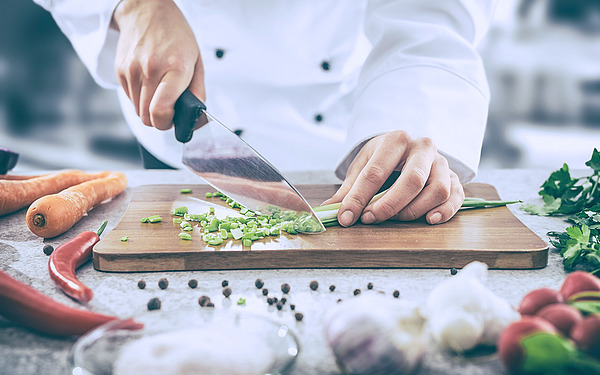 Koch schneidet Kräuter auf einem Holzbrett